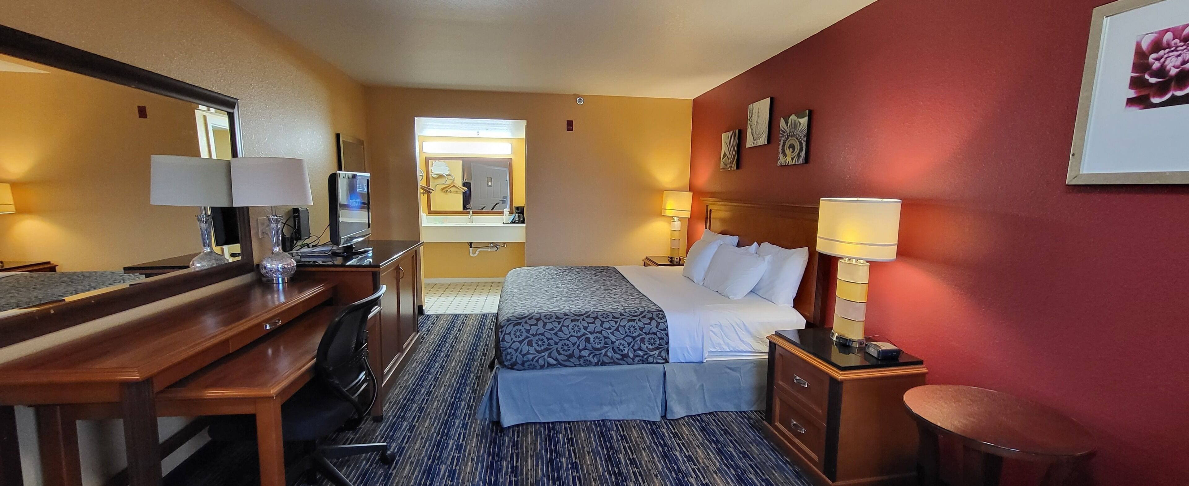 A hotel room with a desk, two beds, a mirror, and a nightstand.