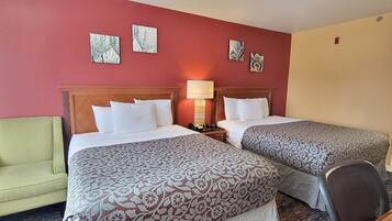 A hotel room with two beds, a green armchair, a bedside table with a lamp, and artwork on the walls.