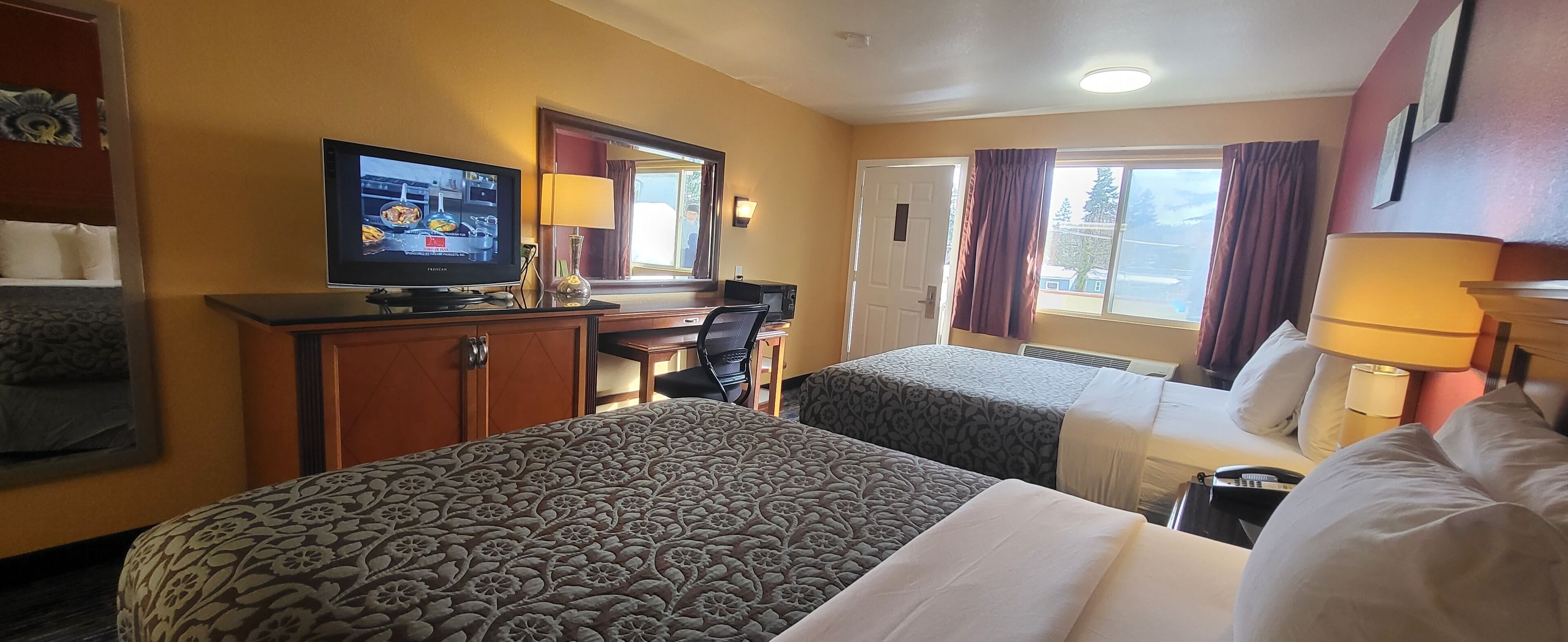 A hotel room with two beds, a television, a desk, and a window with curtains.