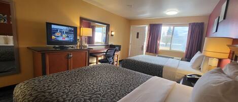 A hotel room with two beds, a television, a desk, and a window with curtains.