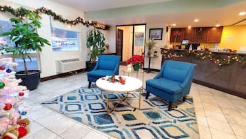 Um saguão de hotel com uma árvore de Natal, dois poltronas azuis, uma mesa redonda e um balcão de recepção.