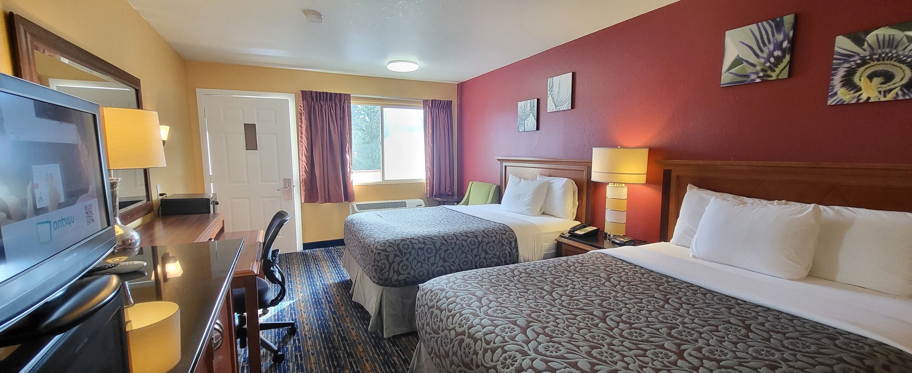 A hotel room with two beds, a desk with a TV, a chair, and a window with curtains.