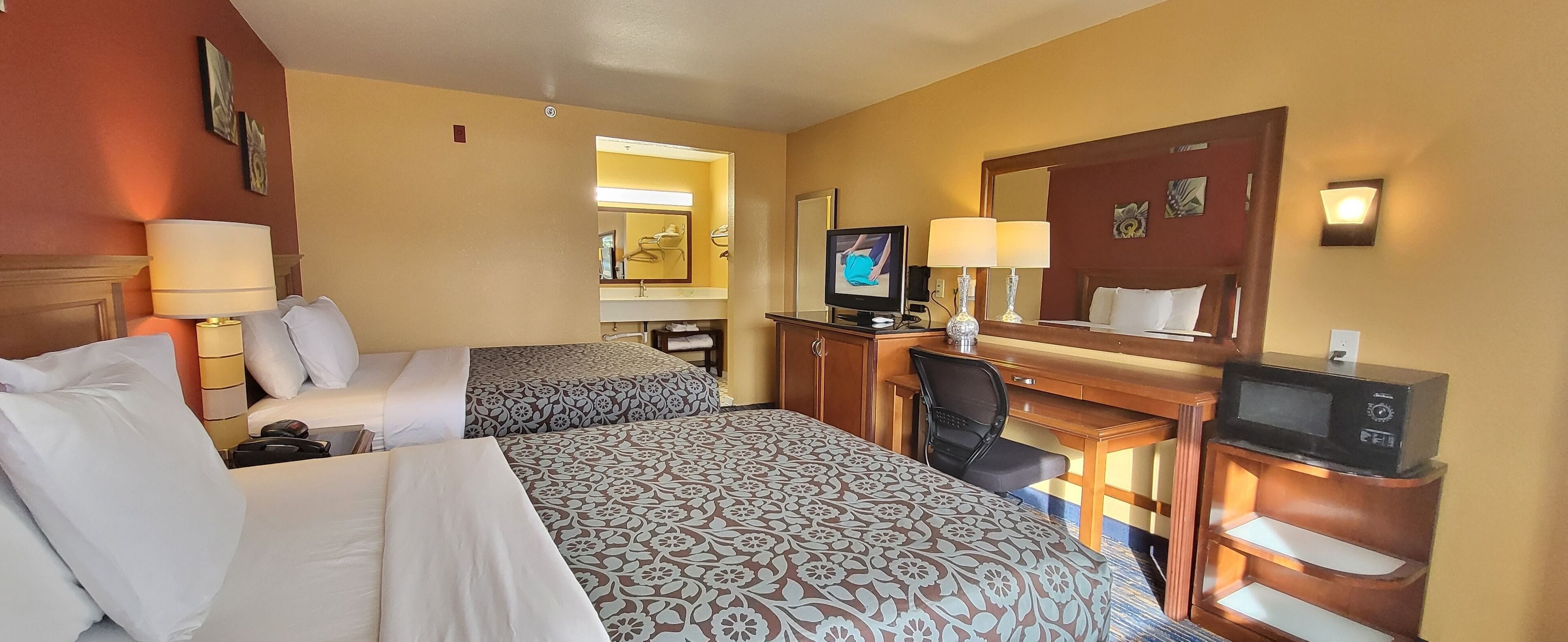 A hotel room with two beds, a desk with a computer, a TV, and a mirror.