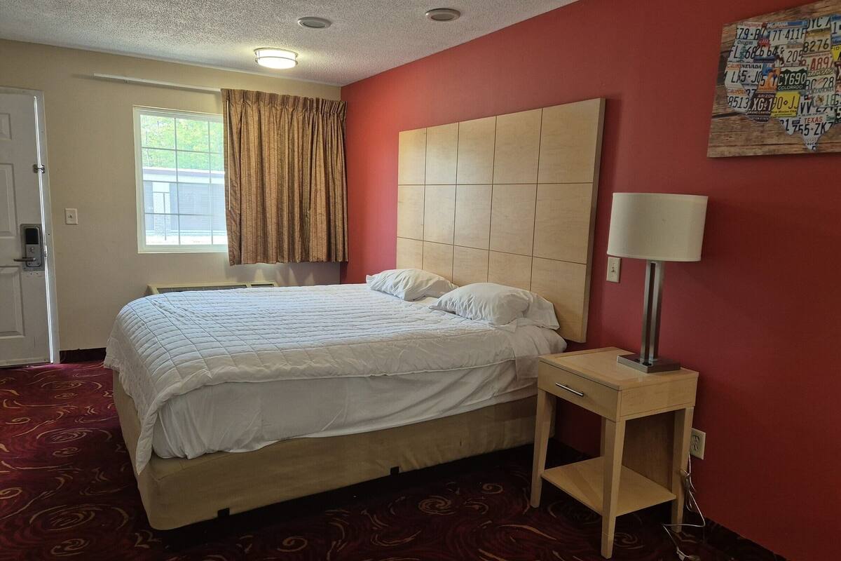 Hotellihuone, jossa on suuri sänky, yöpöytä lampun kanssa, ikkuna, jossa on verhot, ja seinä, jossa on kartta.