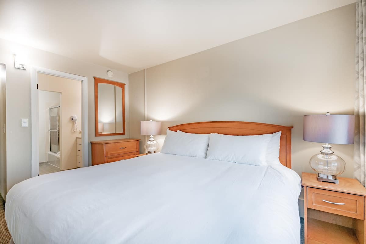 Ein Hotelzimmer mit einem großen Bett, einem Holz-Kopfteil, Nachttischen mit Lampen, einem Spiegel und einer Tür zu einem Badezimmer.