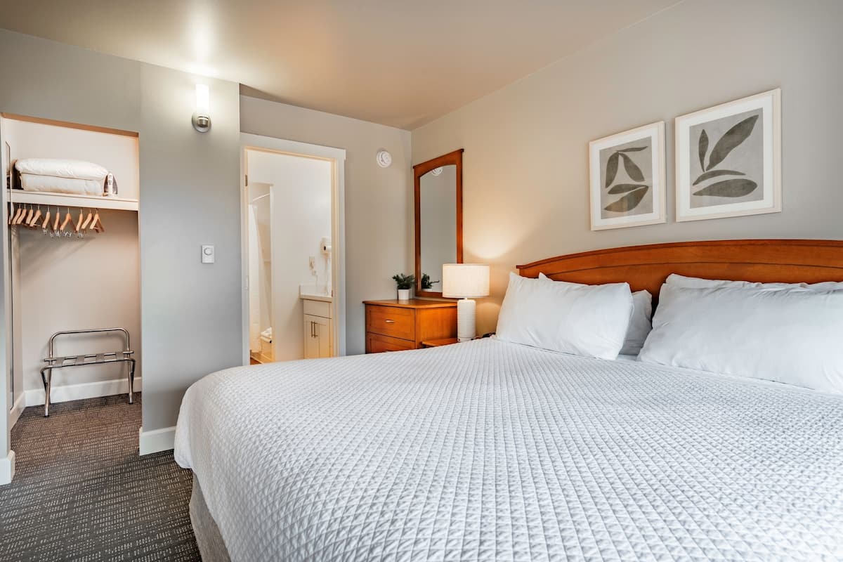Ein Hotelzimmer mit einem großen Bett, einem hölzernen Kopfteil, einem Nachttisch mit Lampe, einem Kleiderschrank und zwei gerahmten Bildern an der Wand.