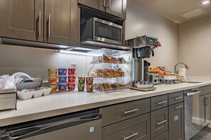 Une cuisine moderne équipée d’appareils électroménagers en acier inoxydable, d’une machine à café et d’un présentoir transparent pour les aliments.