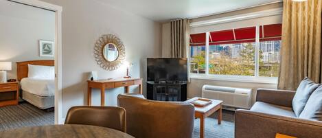 Una habitación de hotel con una cama, televisión, sofá, mesa de comedor y ventana con vista a la ciudad.