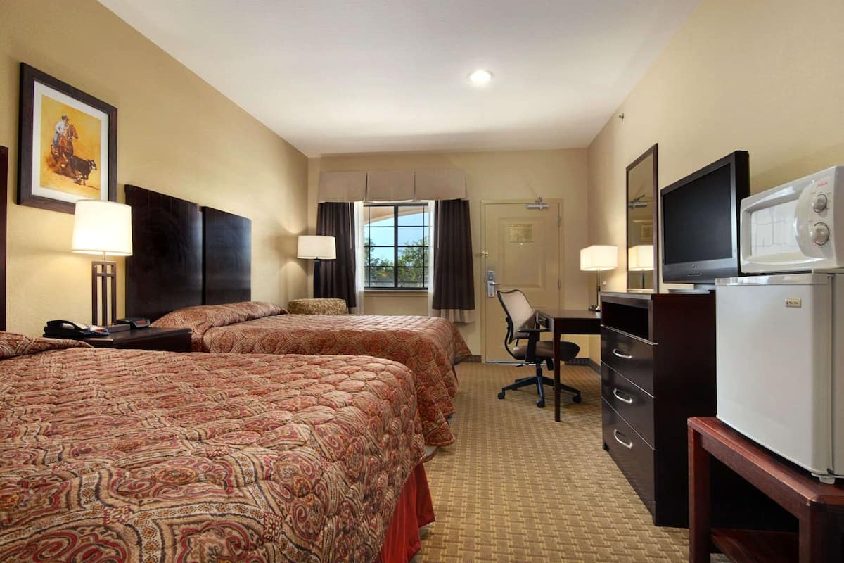 Habitación de hotel con dos camas, un escritorio con silla, televisor, refrigerador y ventana con cortinas.