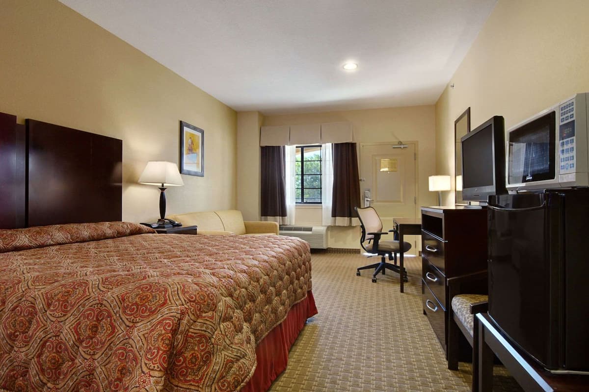 Habitación de hotel con una cama grande, un escritorio con computadora, televisor y ventana con cortinas.