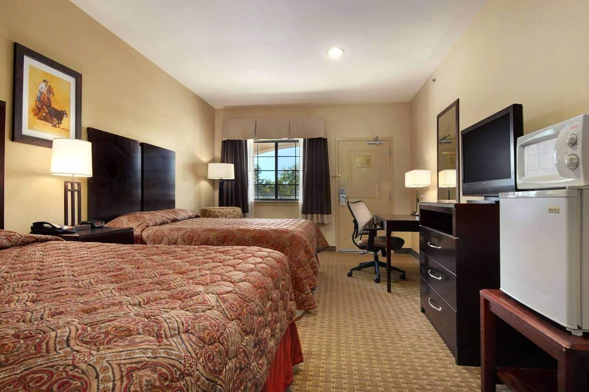 Habitación de hotel con dos camas, un escritorio, televisor y refrigerador.