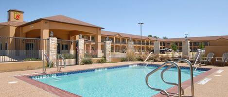 A hotel with a swimming pool, outdoor seating, and a clear blue sky.