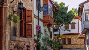 A cobblestone street lined with traditional buildings, a bicycle parked by the side, and directional signs. - Hotel Lunay (Konyaalti)