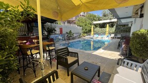 An outdoor seating area with tables and chairs under a yellow umbrella, a pool, and a small garden area. - Hotel Lunay (Konyaalti)