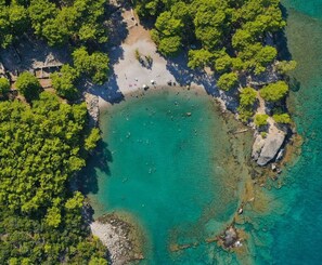 An aerial view of a beach with clear turquoise water, surrounded by dense green foliage and rocky outcrops. - Hotel Lunay (Konyaalti)
