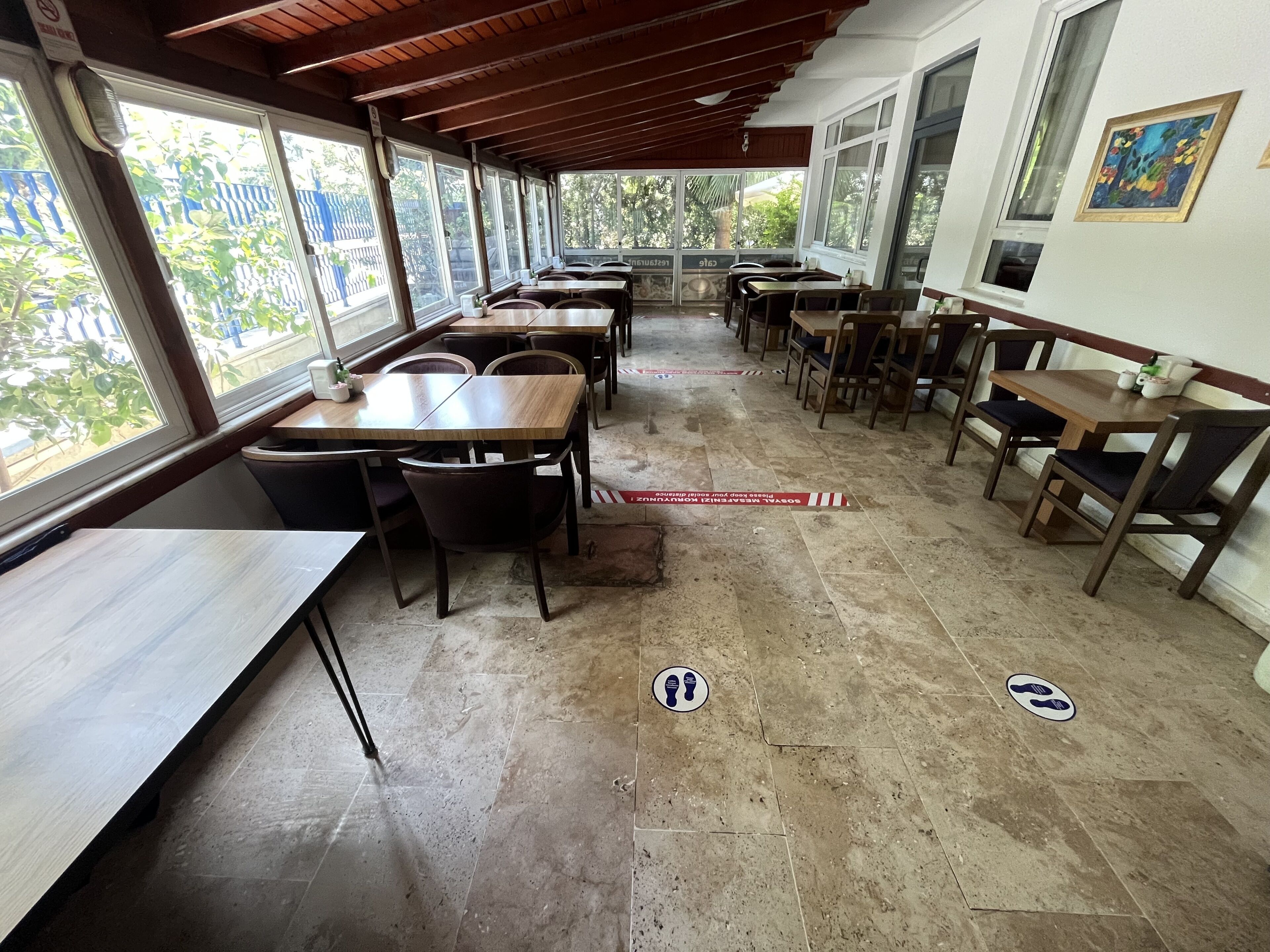 A restaurant with multiple tables and chairs, large windows, and a tiled floor.