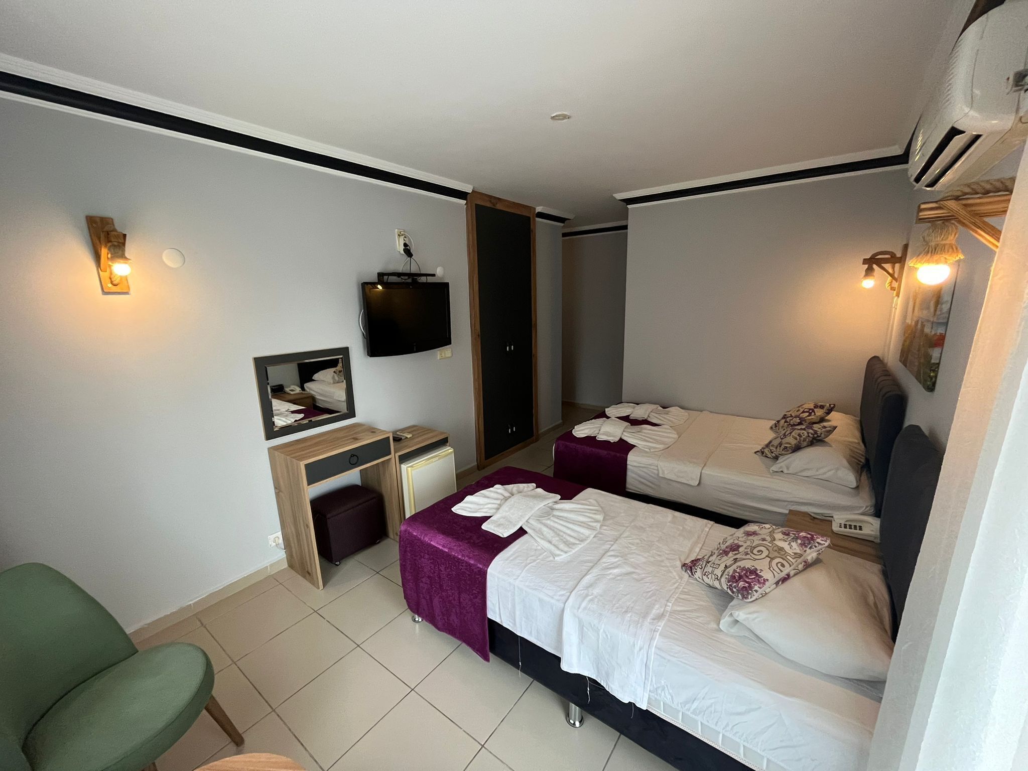 A hotel room with two beds, a desk, a chair, a TV, and a wardrobe.