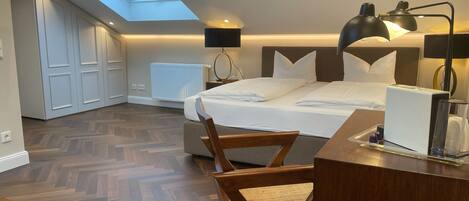 Ein modernes Hotelzimmer mit Dachfenster, einem Bett mit weißer Bettwäsche, einem Schreibtisch mit Lampe und einem Sessel.