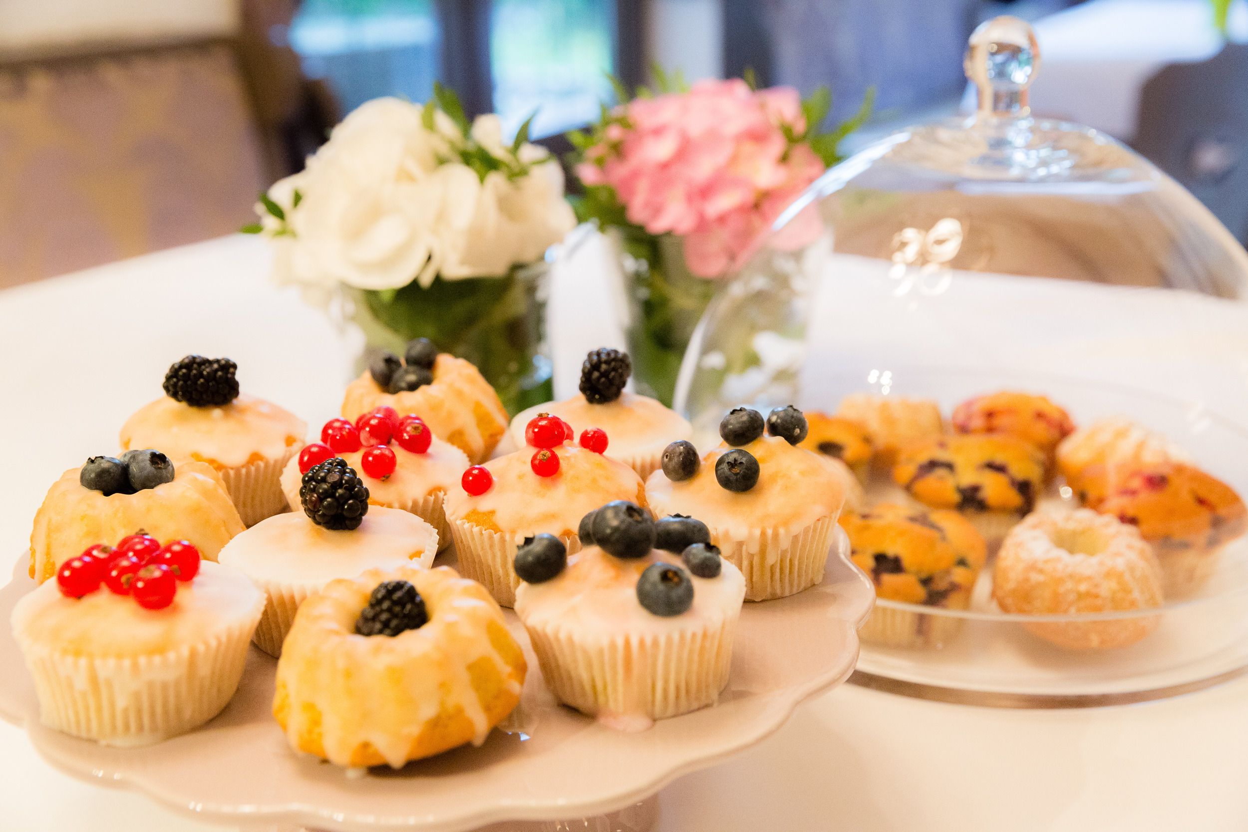A variety of pastries on a white plate, including cupcakes with berries and a glass display case with more pastries.