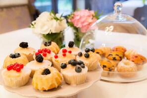 Une variété de pâtisseries est présentée sur une assiette blanche, notamment des cupcakes aux fruits rouges, et une vitrine en verre expose d’autres pâtisseries.