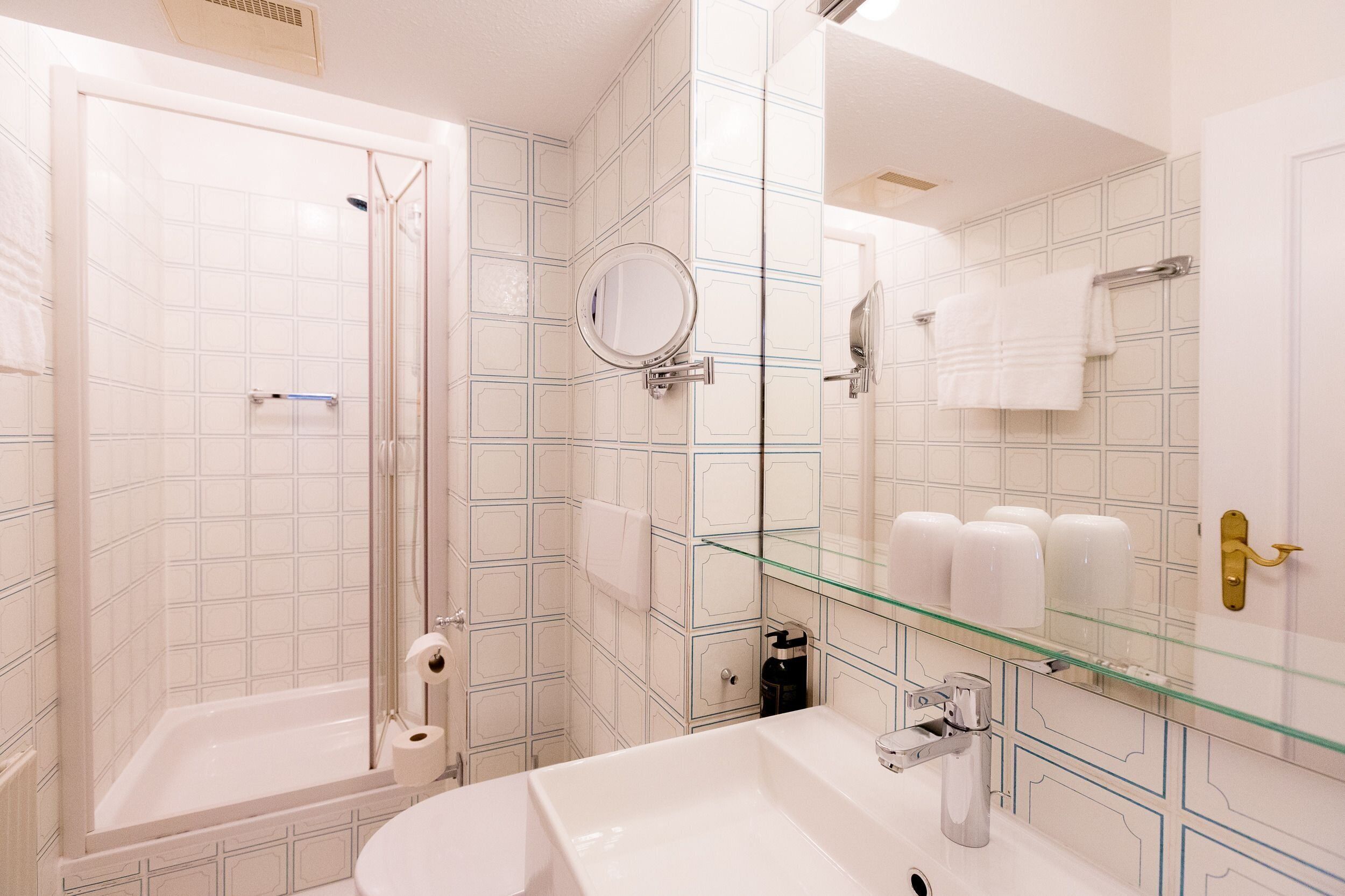 A modern bathroom with a glass shower enclosure, a white sink, and a glass-topped vanity.