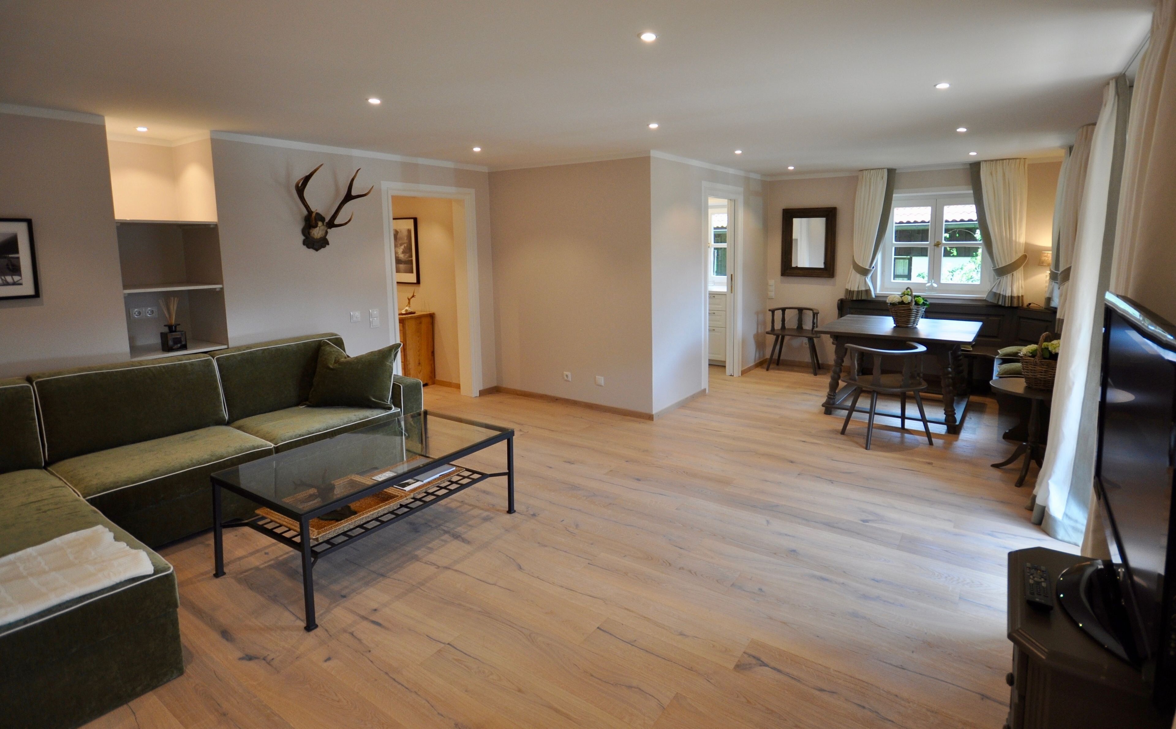 A spacious living area with a green sofa, a glass coffee table, and a wooden dining table with chairs.