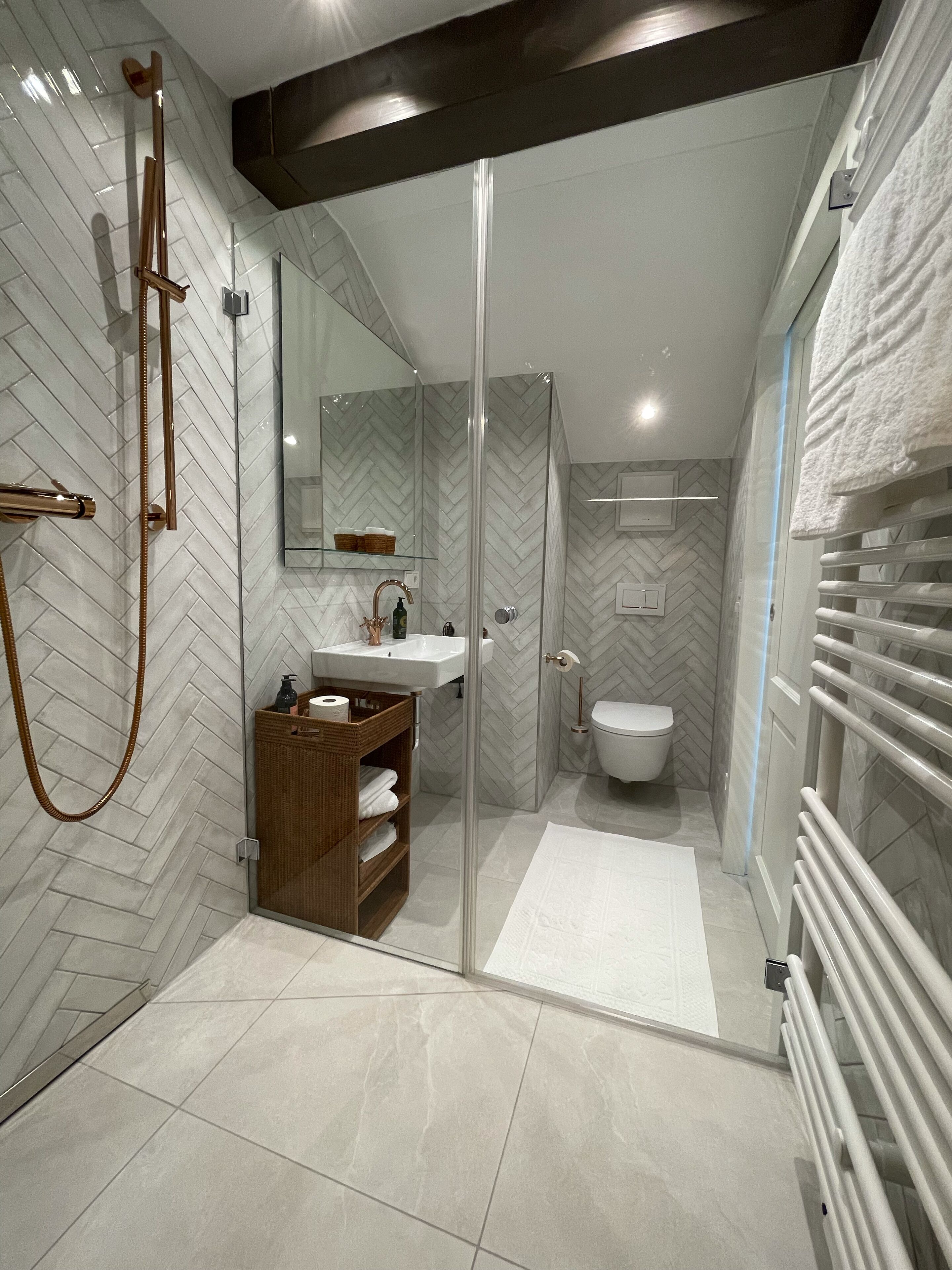 A modern bathroom with a herringbone tile pattern, a glass-enclosed shower, a wooden vanity, and a white toilet.