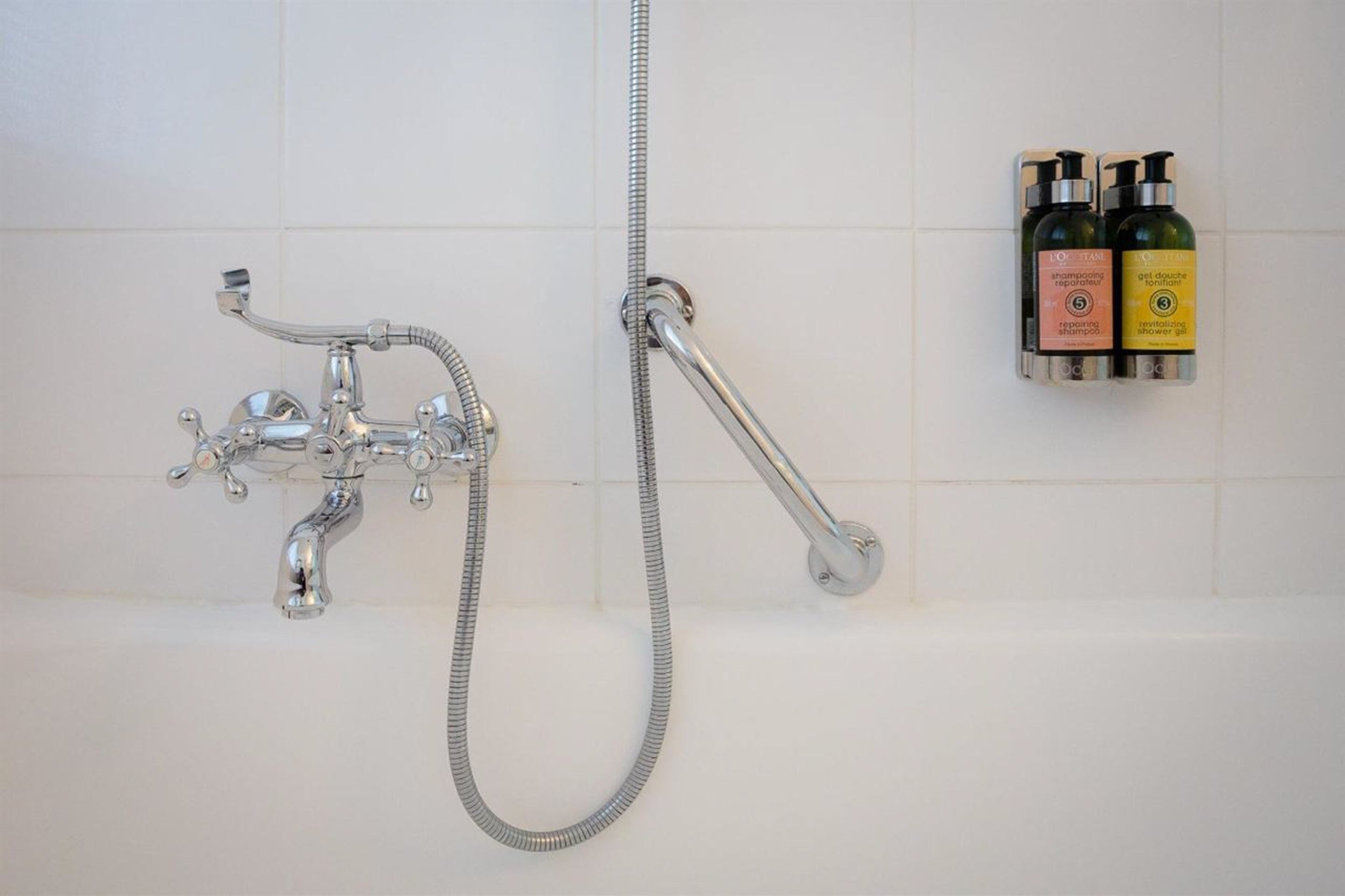 Un bagno con doccia, soffione a mano e due flaconi di shampoo e bagnoschiuma a parete.