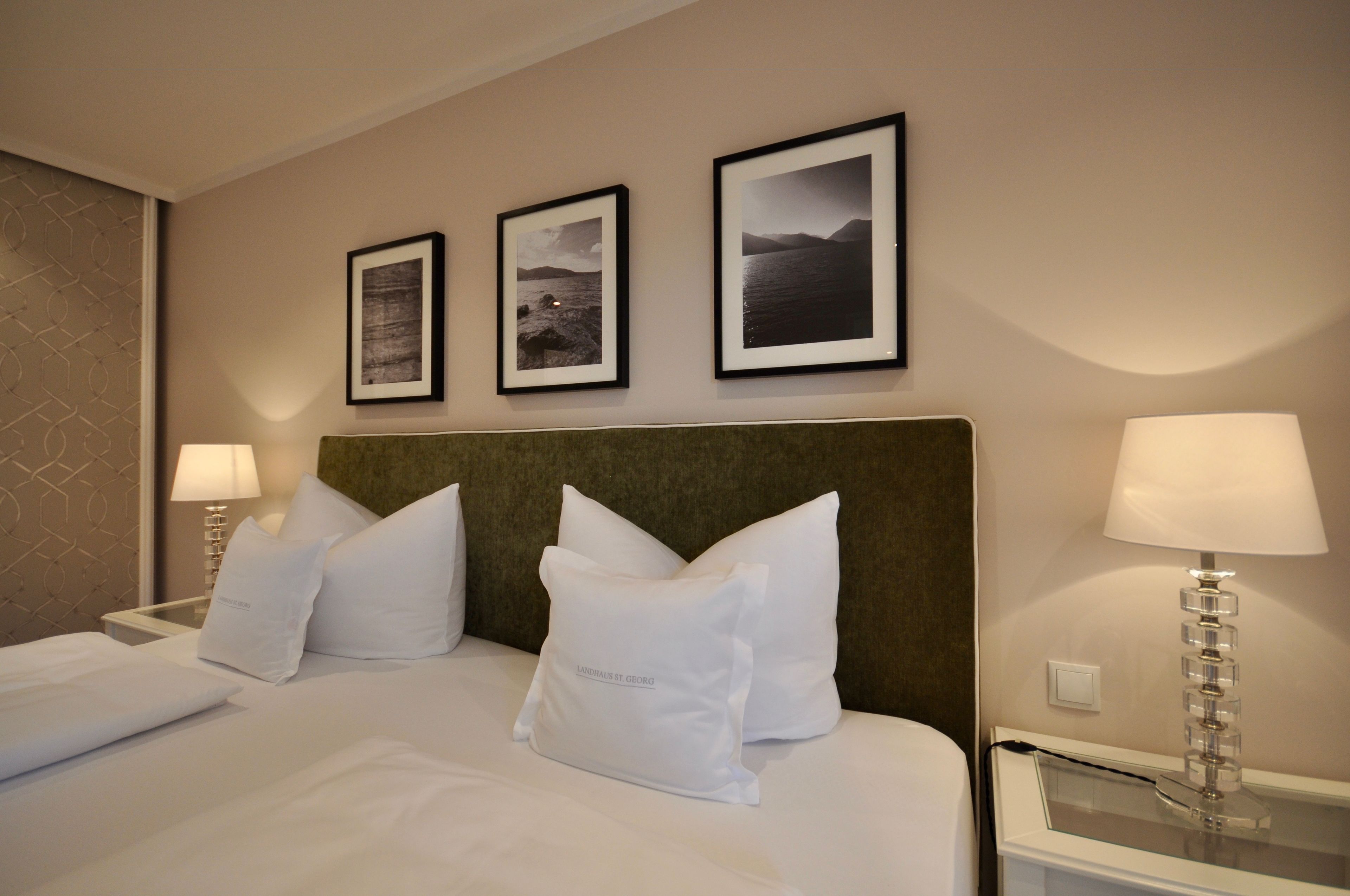 A hotel room with a bed, two white pillows, a headboard, and three framed pictures on the wall.
