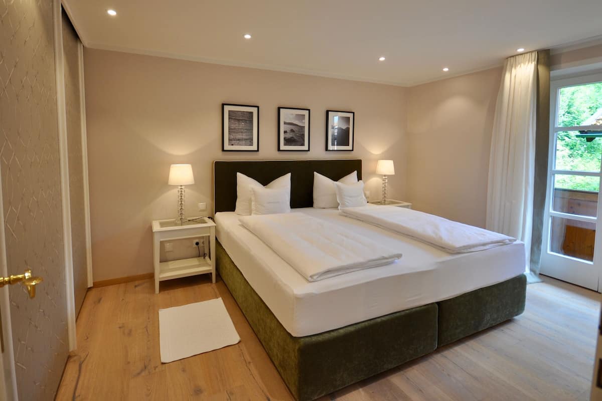 A hotel room with a large bed, two bedside tables with lamps, a window with curtains, and three framed pictures on the wall.