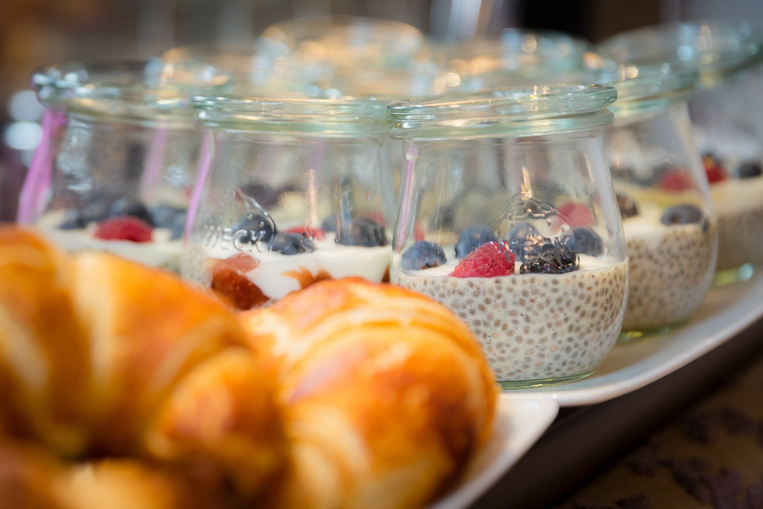 Un plateau contenant divers aliments, notamment un croissant et des verrines de pudding aux graines de chia, garnies de fruits rouges.