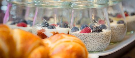 Un plateau contenant divers aliments, notamment un croissant et des verrines de pudding aux graines de chia, garnies de fruits rouges.