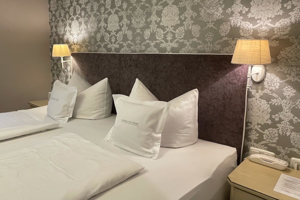 A hotel room with a bed, pillows, a nightstand, a lamp, and a phone.