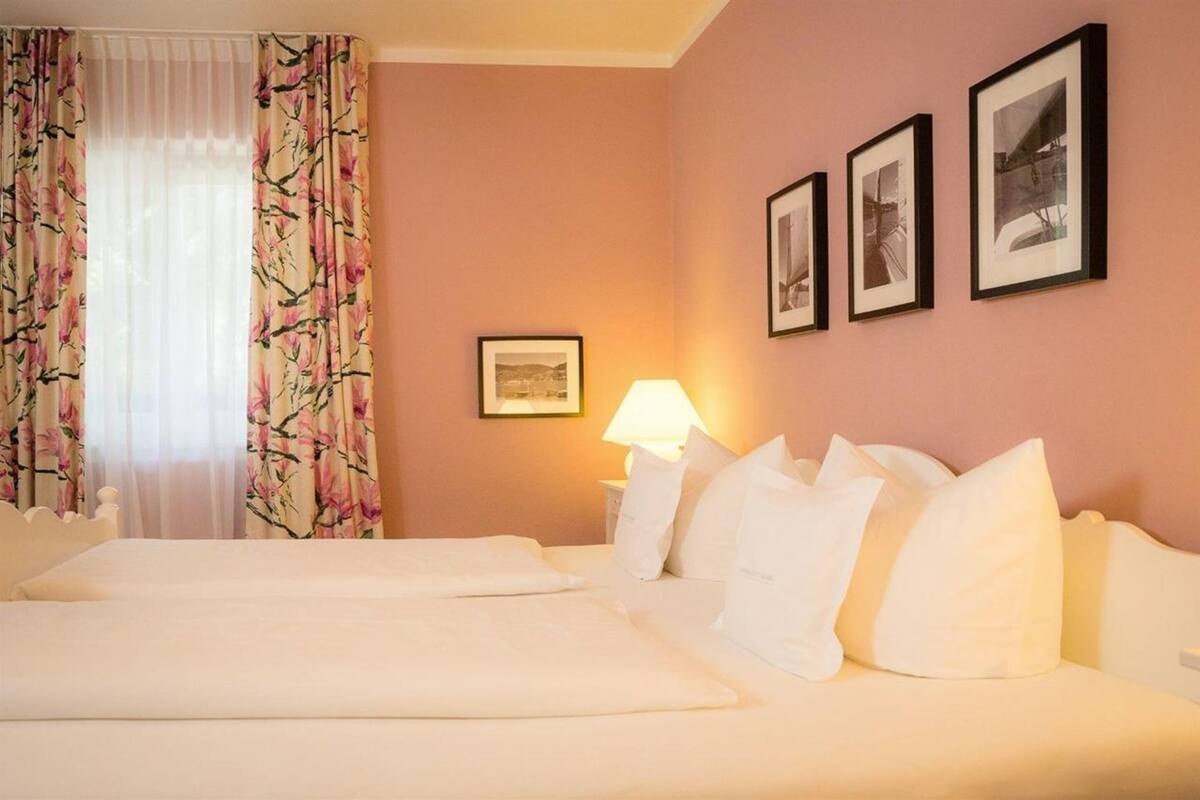 A hotel room with two beds, a nightstand with a lamp, and three framed pictures on the wall.
