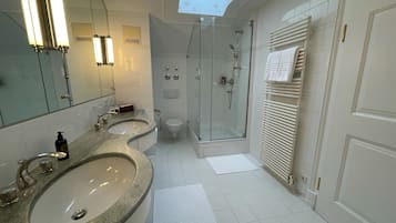 Un bagno moderno con due lavabi, cabina doccia in vetro, finestra a lucernario e portasciugamani.