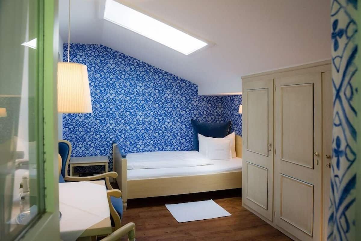 A small room with a bed, a chair, a table, and a wardrobe.