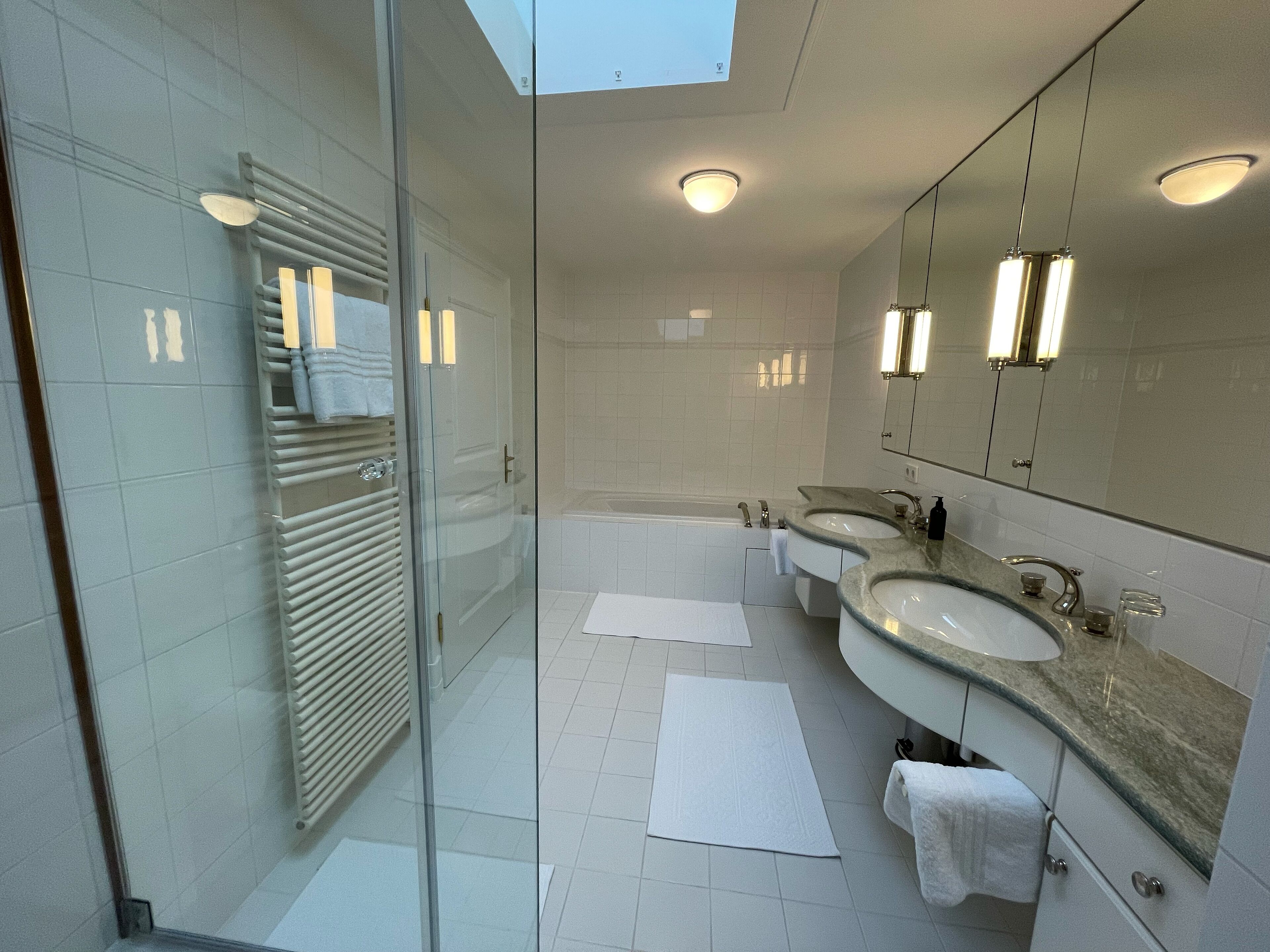 Un baño moderno con cabina de ducha de vidrio, un espejo grande y dos lavamanos.