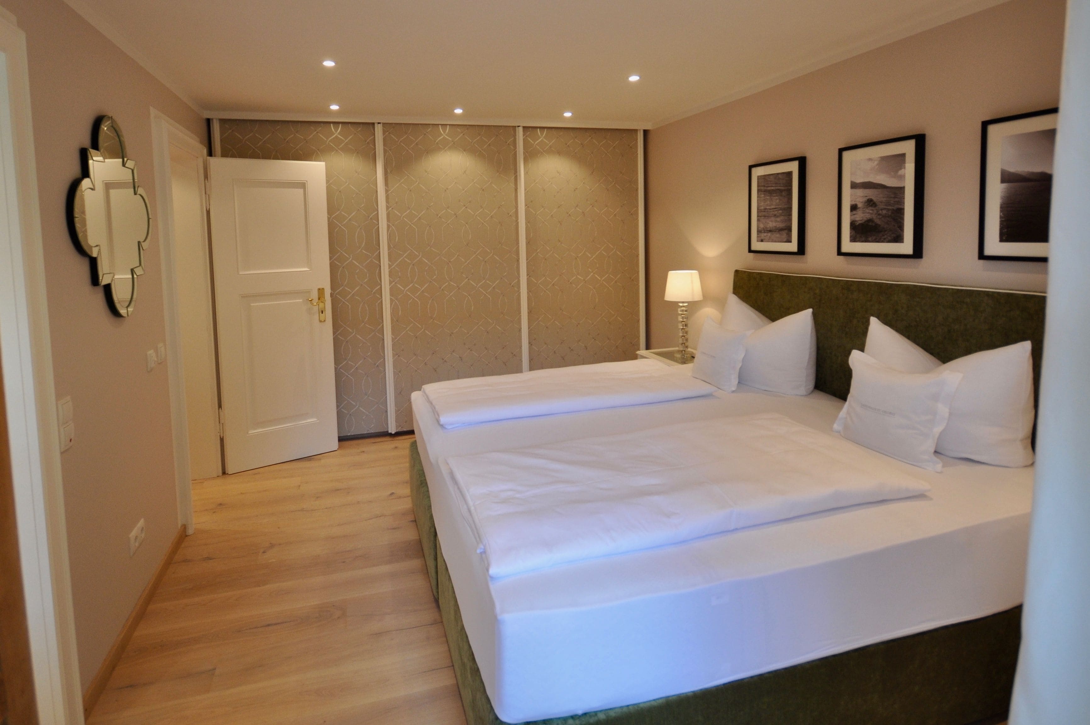 A hotel room with two beds, a door, a mirror, and wall-mounted pictures.