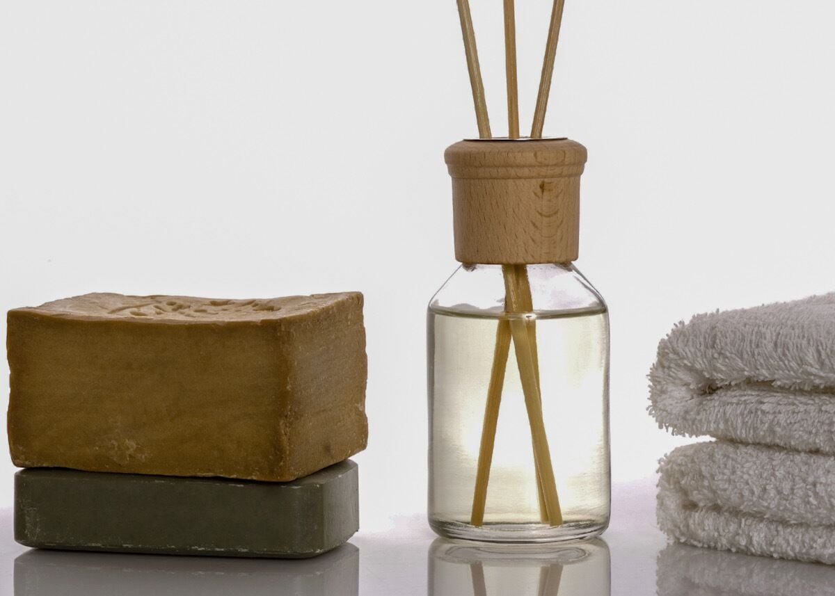 A bar of soap, a glass bottle with reed sticks, and a folded towel.