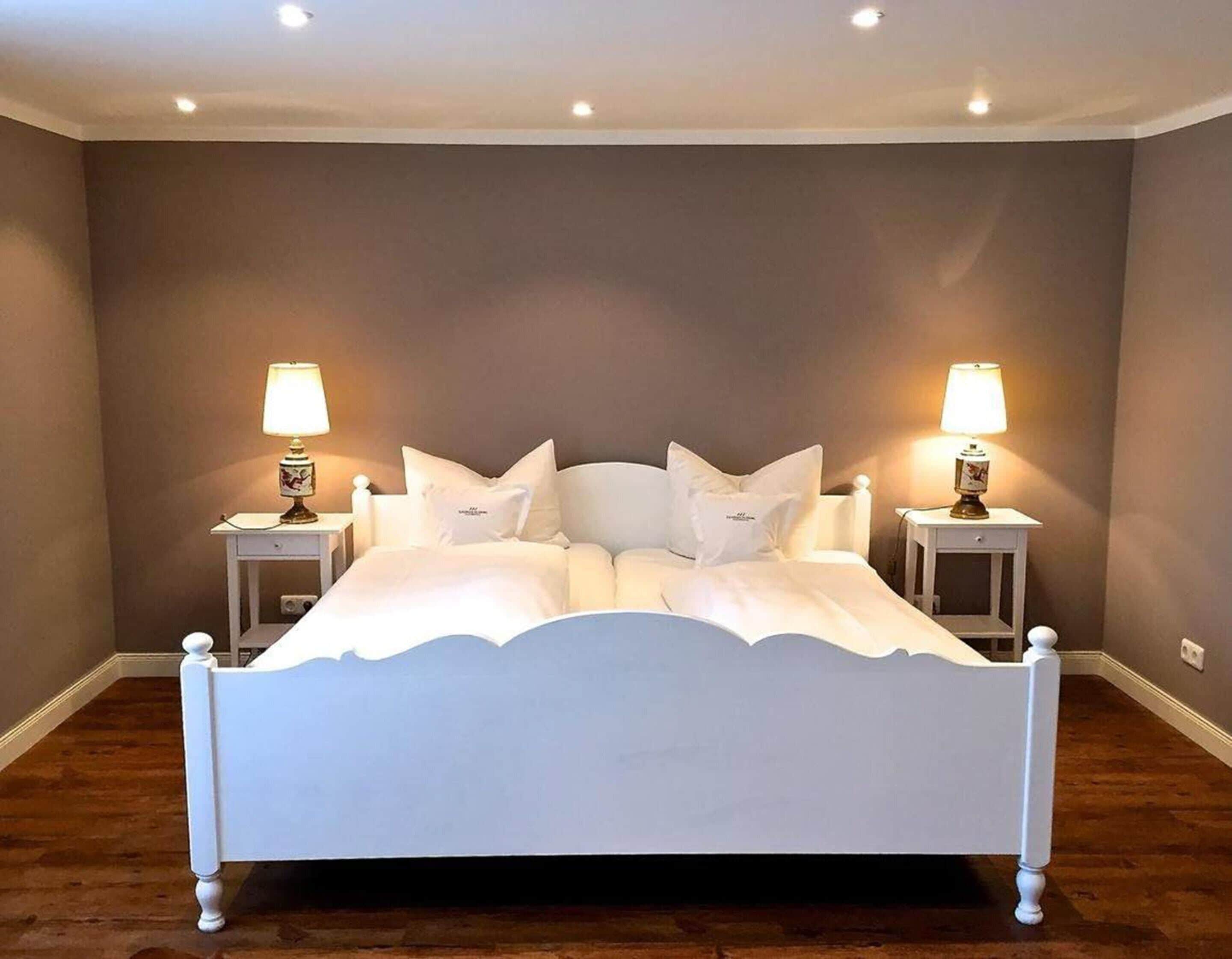 A bedroom with a white bed, two bedside tables with lamps, and a brown wall.