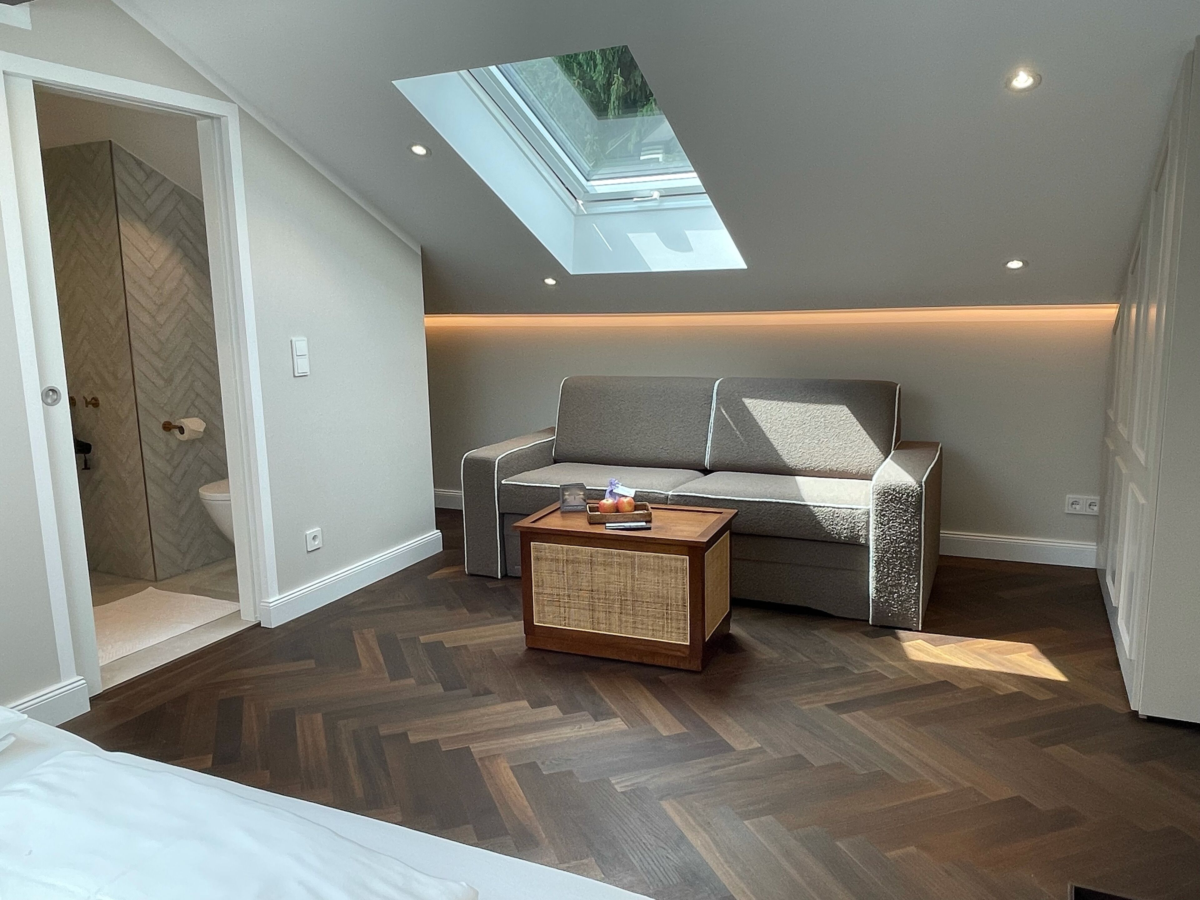 A modern living room with a skylight, a grey sofa, a wooden coffee table, and a herringbone-patterned floor.