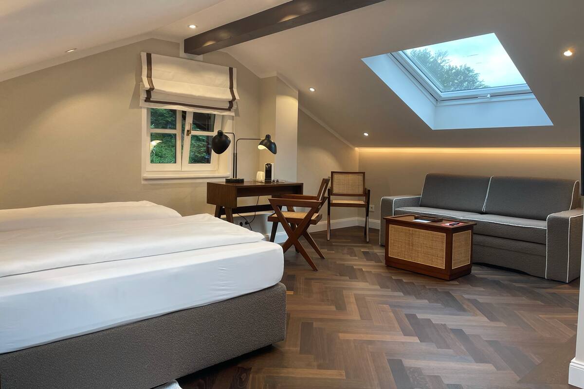 A modern bedroom with a skylight, a bed, a desk, and a sofa.