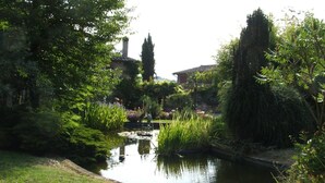 A serene garden with a pond, lush greenery, and a traditional building in the background. - Hotel Il Pietreto (Colle di Val d'Elsa)