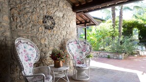 A stone wall with wicker chairs and a table, surrounded by greenery and a tiled patio. - Hotel Il Pietreto (Colle di Val d'Elsa)