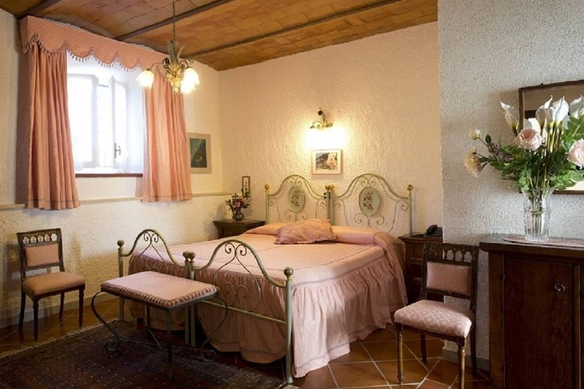 Une chambre à coucher avec un lit, deux chaises, une table de chevet, une commode et une fenêtre avec des rideaux.