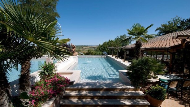 A swimming pool with steps leading down to it, surrounded by tropical plants and a pergola. - Hotel Il Pietreto (Colle di Val d'Elsa)
