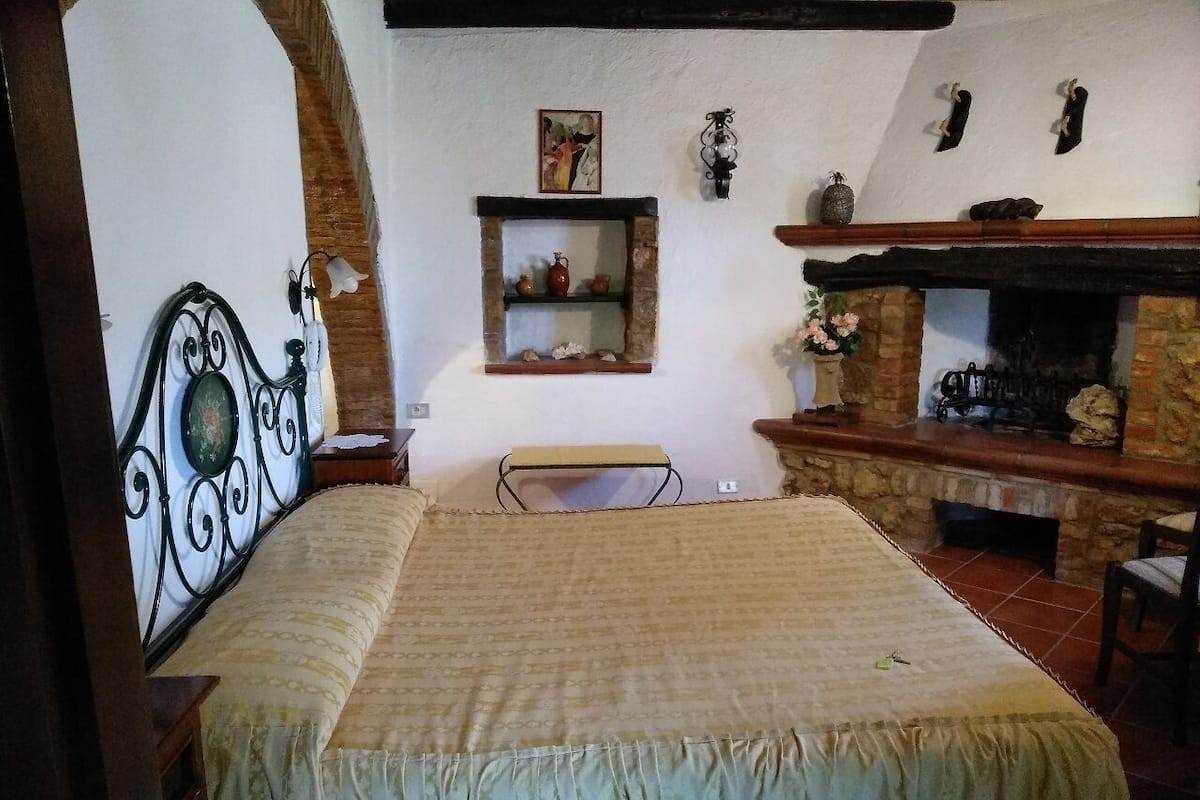 Une chambre à coucher comprenant un lit, une petite table, une étagère avec des objets décoratifs et une cheminée.