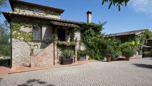 A rustic stone building with a tiled roof, ivy-covered walls, and a chimney. There are potted plants and a paved courtyard. - Hotel Il Pietreto (Colle di Val d'Elsa)