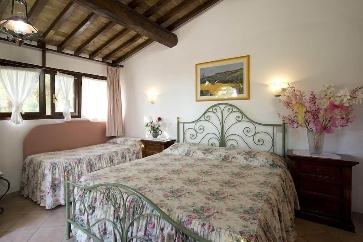 Une chambre avec deux lits simples, un plafond en bois, un tableau encadré au mur et un vase de fleurs posé sur une table de chevet.