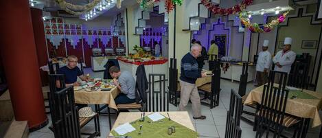 Um restaurante com mesas postas para refeições, um balcão com alimentos e uma decoração festiva no teto.